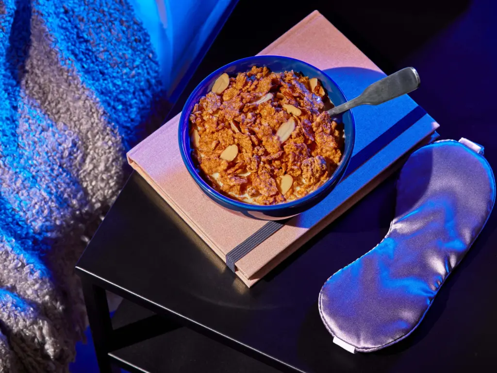 a bowl of Sweet Dreams cereal next to a bed and an eye mask