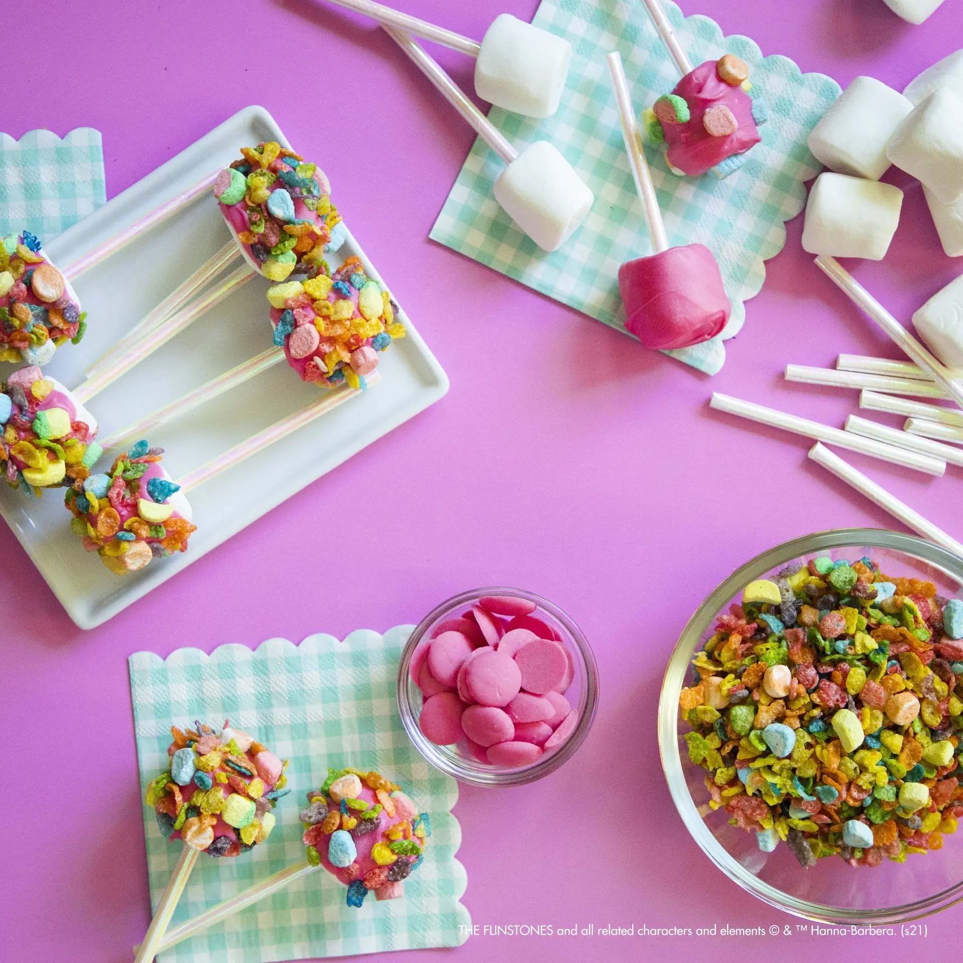 Marshmallow Fruity PEBBLES pops on napkins atop a pink table.