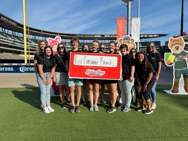 A group of people stand on a football field and hold up a sign that says Post Consumer Brands