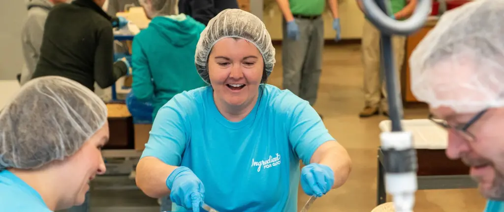 A woman in a Post shirt and hairnet scoops material into a container.