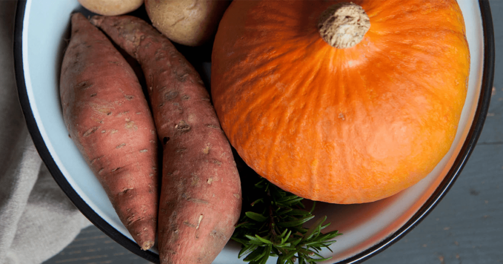 A pumpkin, two sweet potatoes and a sprig of rosemary in a bowl