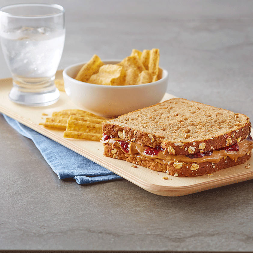 Peanut Butter and Jelly Sandwich next to a bowl of chips and a glass of water.