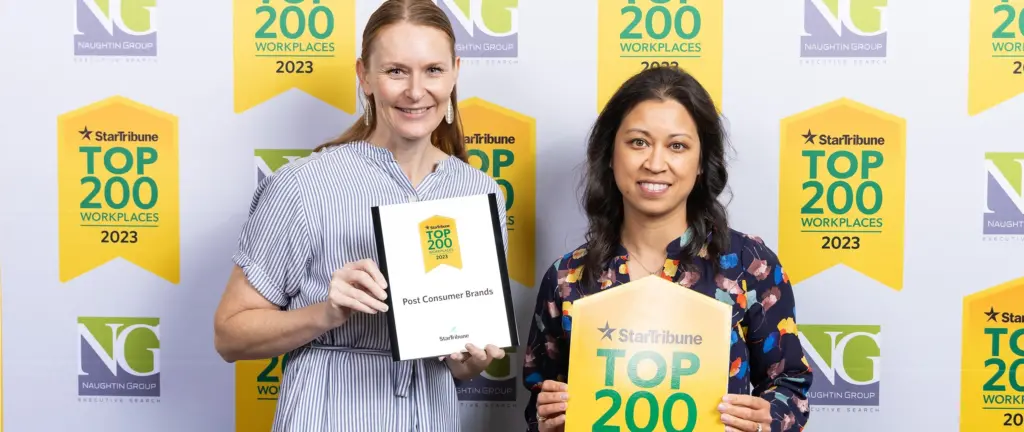 Two people standing in front of a banner while holding up awards.