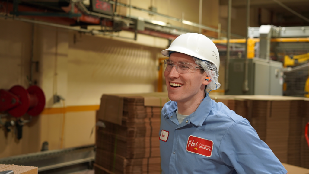 An employee in a hardhat stands in a warehouse