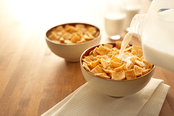 Pouring milk into a bowl of cinnamon squares cereal