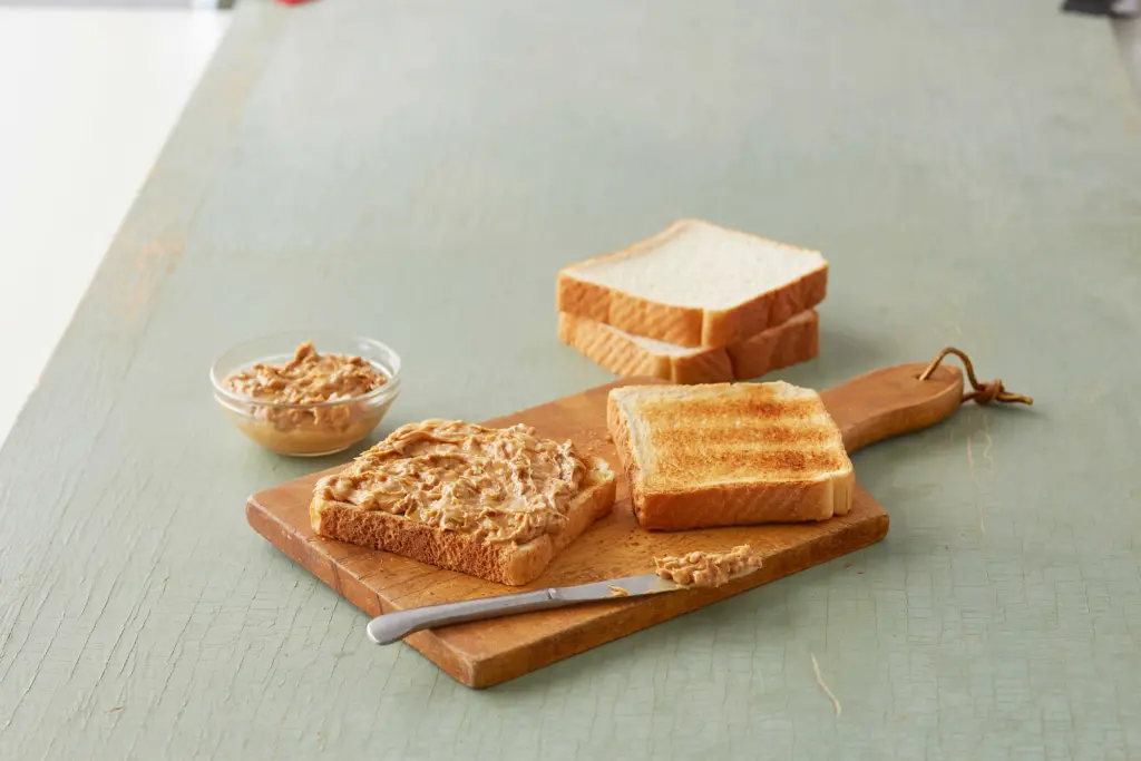 Toast covered with peanut butter on a cutting board next to a bowl of peanut butter.