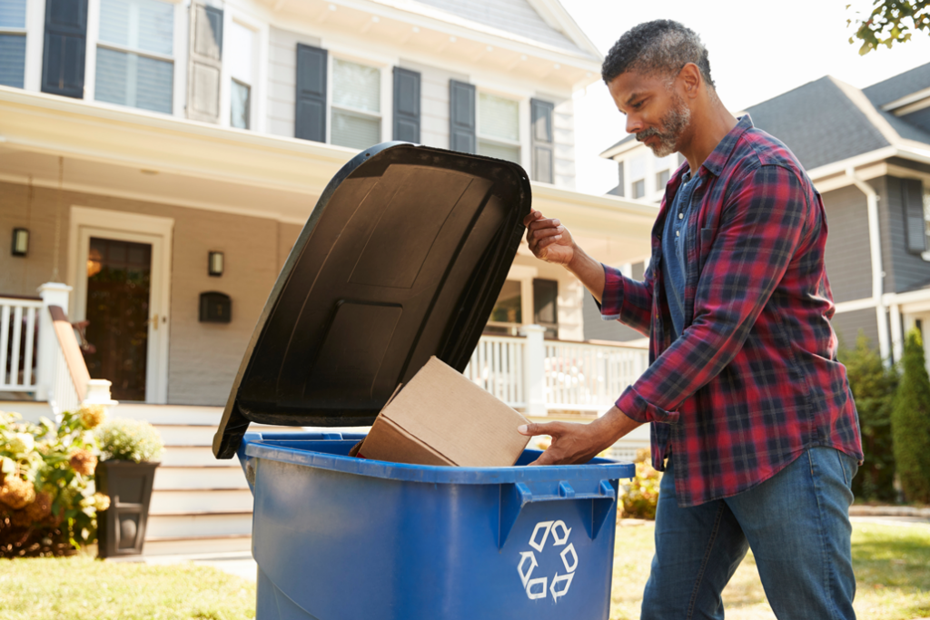 A man putting a cardboard box into a recycling can