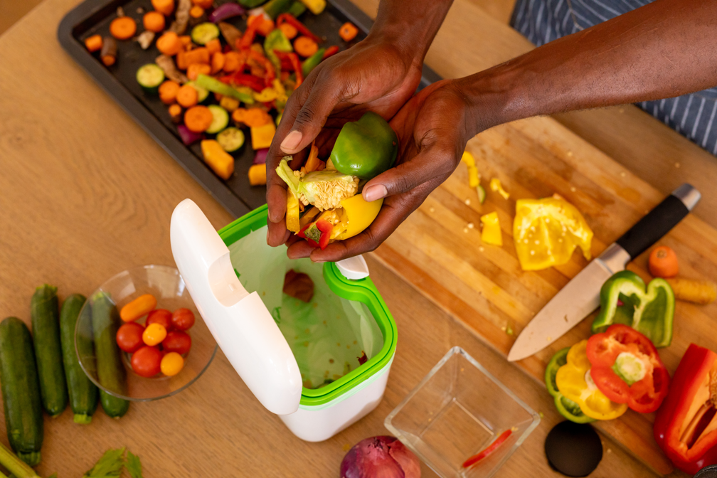 A person putting vegetable scraps into a waste container.