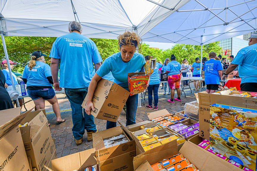 A woman in a blue shirt sets a box down next to boxes filled with Post cereals