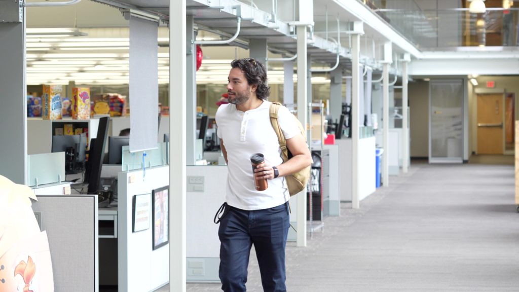 A man with a coffee cup and backpack walks in a Post Consumer Brands office.