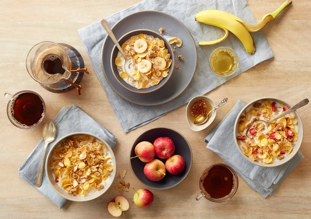 Honey Bunches of Oats cereal varieties in bowls surrounded by fruit on a counter top