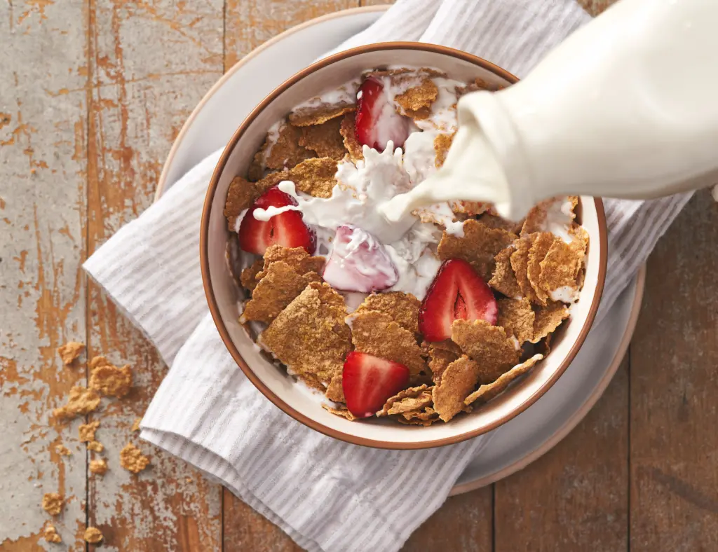 Pouring milk into a bowl of Bran Flakes with strawberries