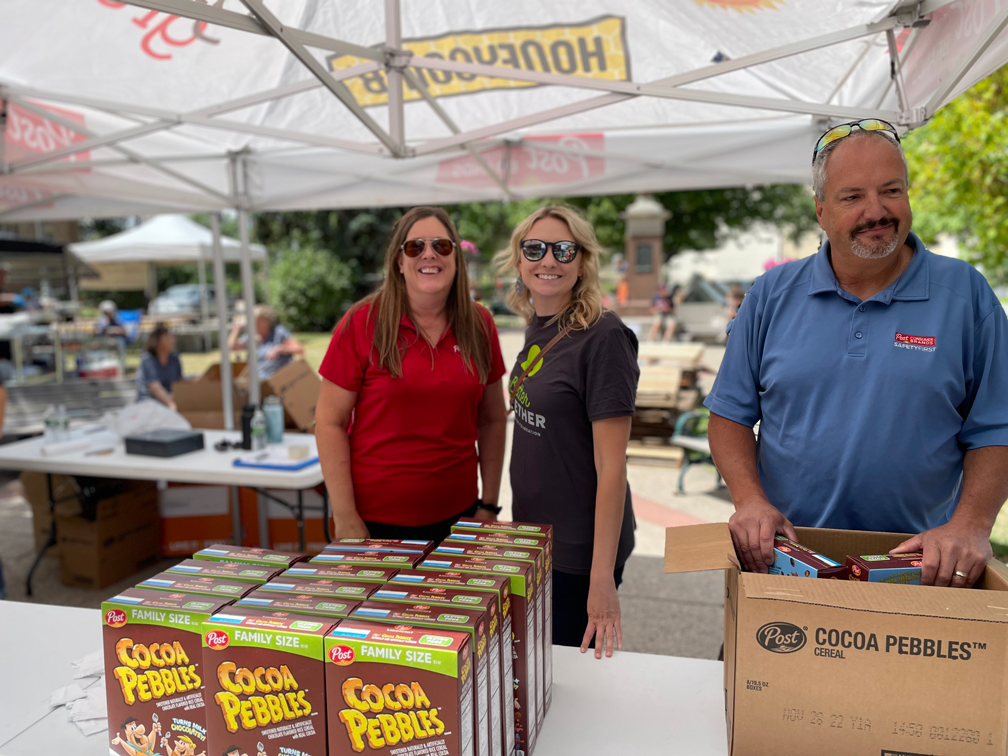 Three people stand in front of a table holding boxes of Cocoa PEBBLES