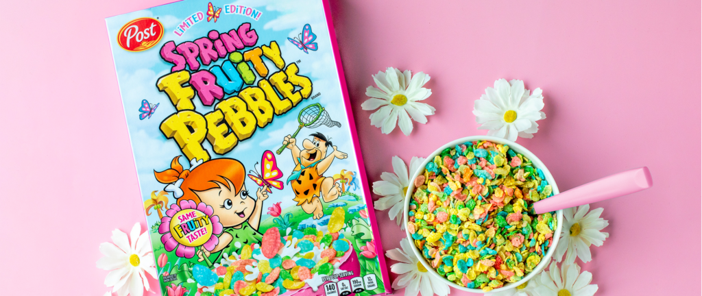 A Spring Fruity PEBBLES box next to a bowl full of cereal surrounded by daisies on a pink background