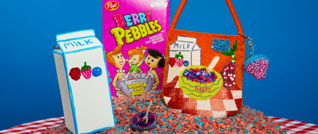 A milk box, box of Berry PEBBLES cereal and a bag and other cereal-inspired accessories designed by Susan Alexandra sitting on top of a pile of Berry PEBBLES cereal pieces.