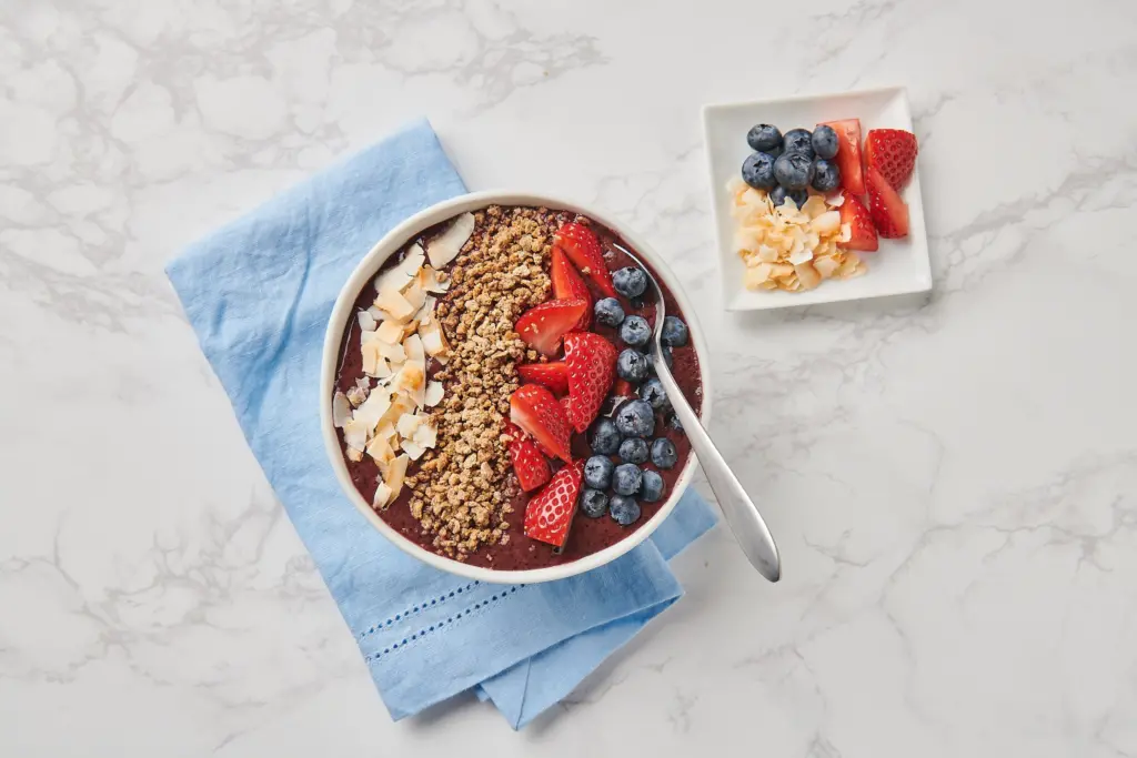An acai bowl with granola, dried coconut, strawberries and blueberries