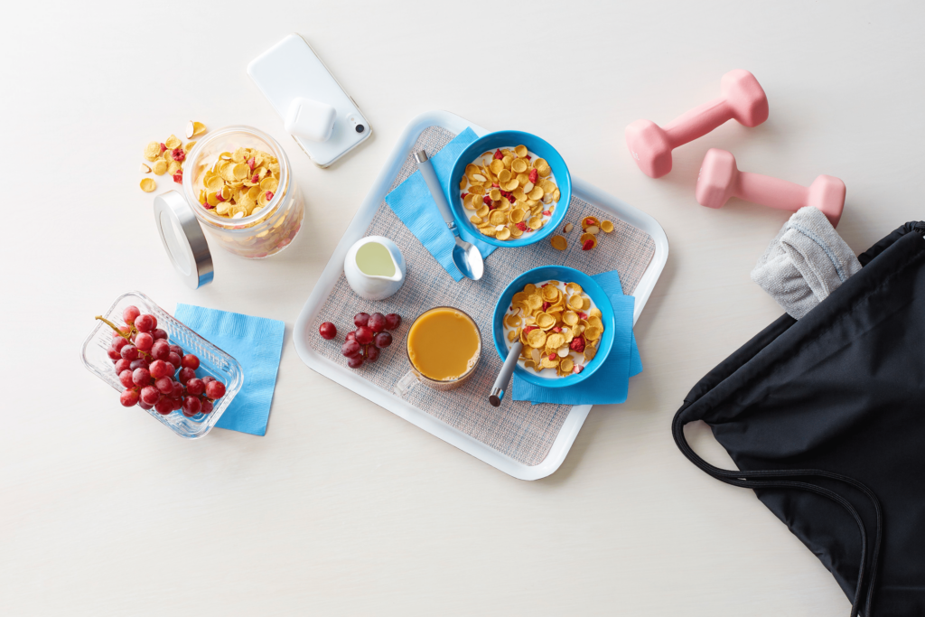 Two bowls of Premier Protein Cereal with a glass of orange juice and grapes on a tray surrounded by a phone and a bag of workout gear