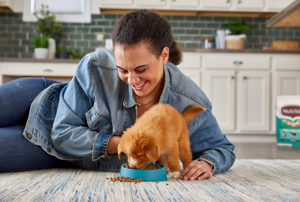 A woman feeds a puppy Nutrish dog food
